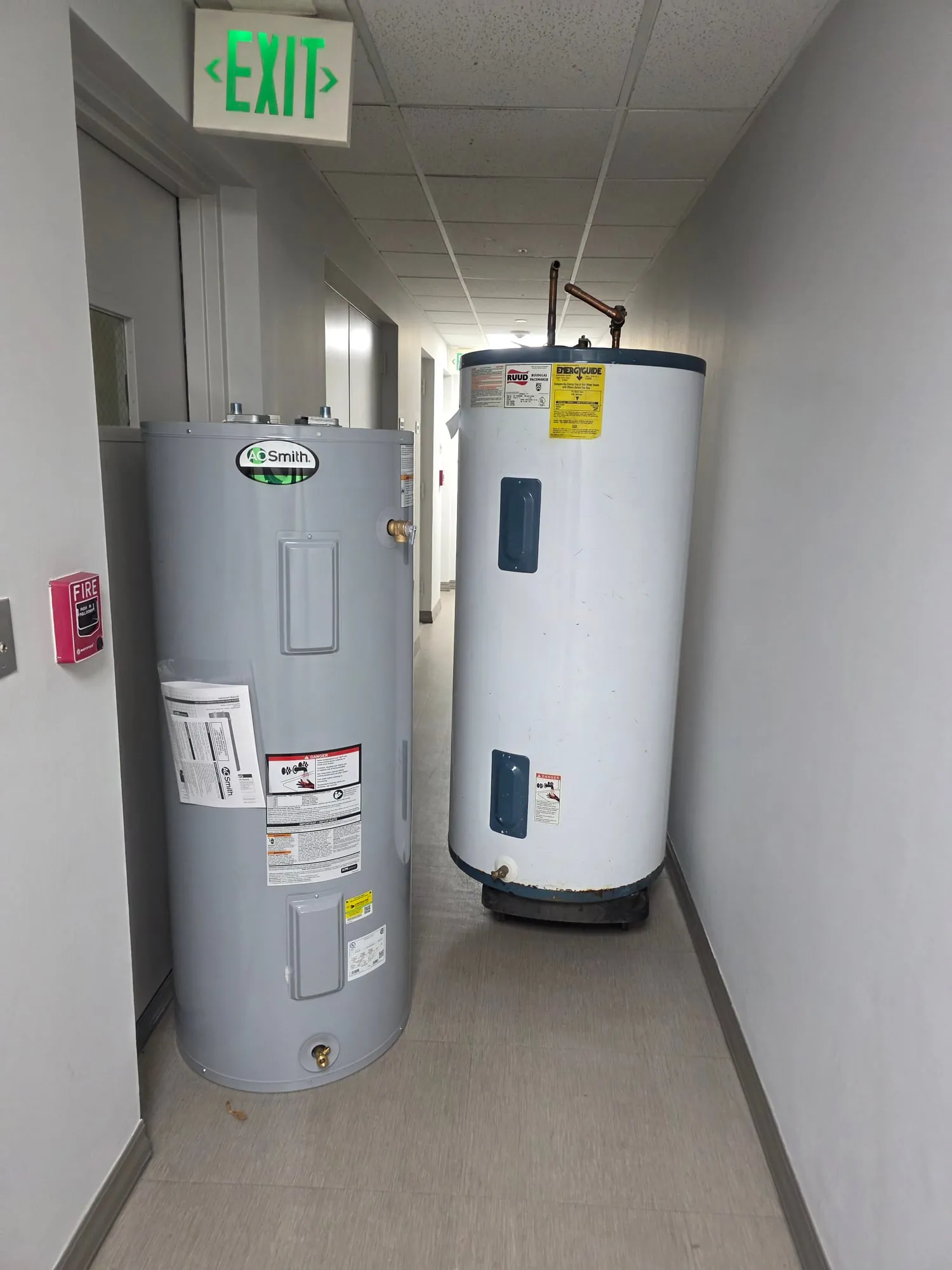 Two commercial electric water heaters in a building service hallway