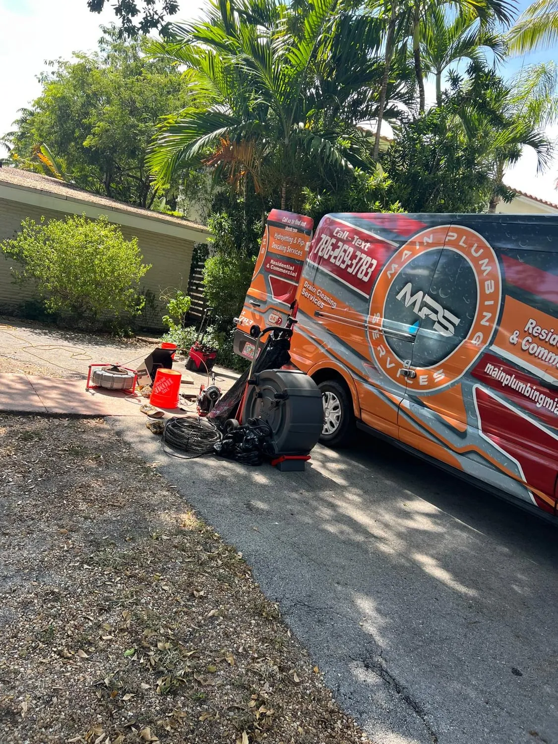Drain cleaning machine and cables set out beside a service van under palm trees