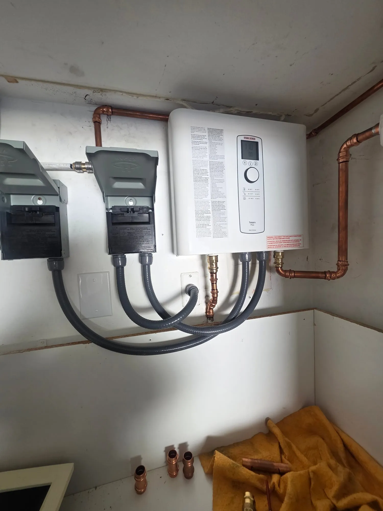 Electric tankless water heater mounted on a wall with two disconnects and copper piping