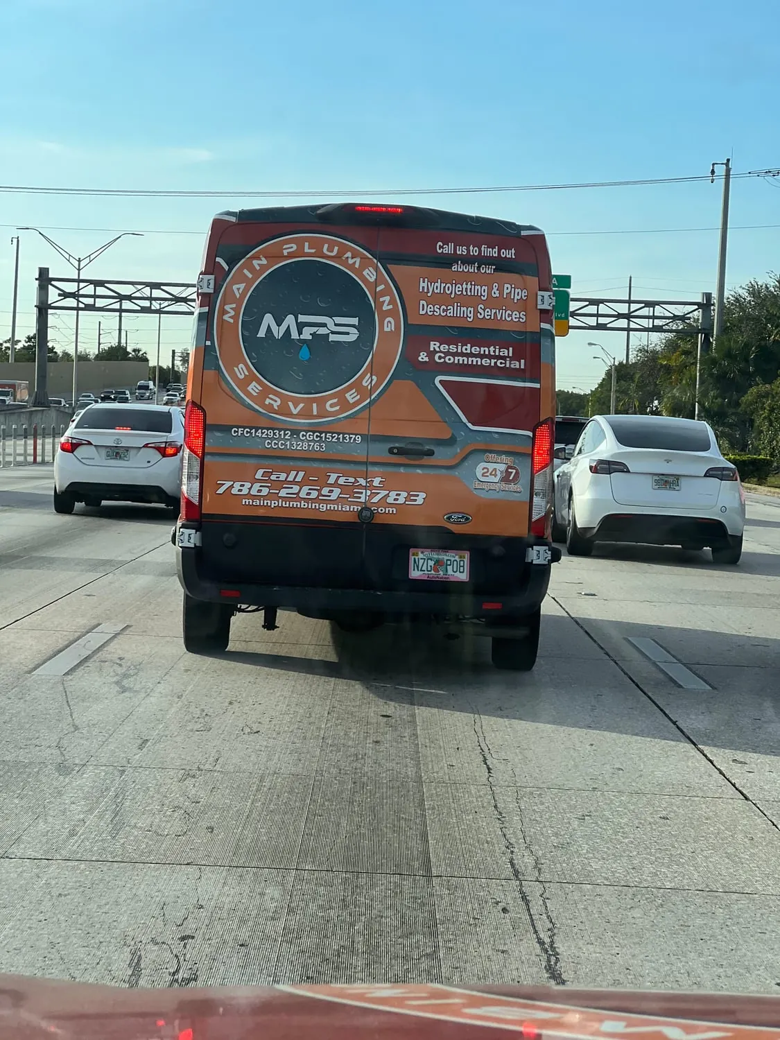 Rear of a Main Plumbing Services van on the highway showing the phone number