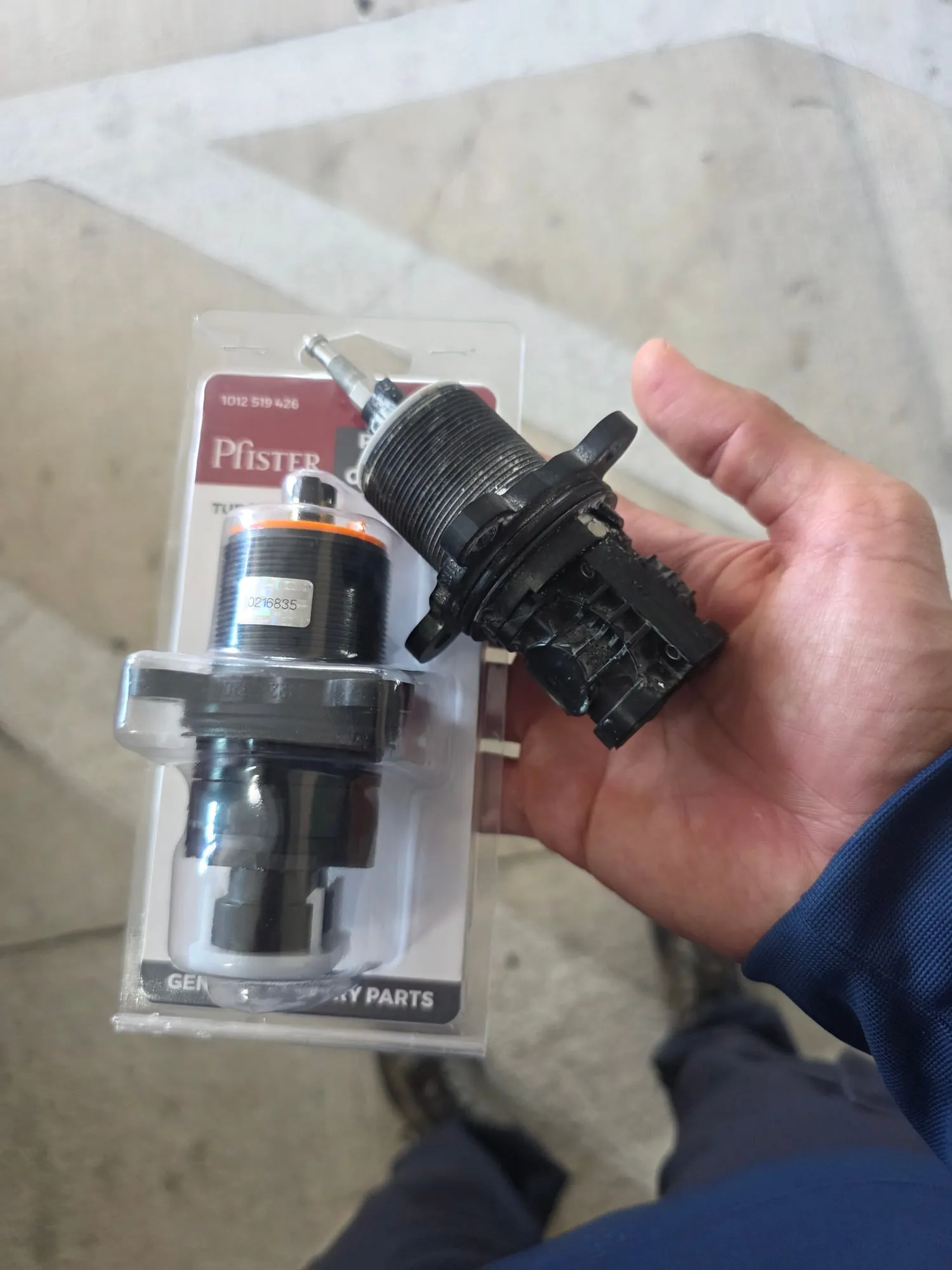Hand holding a worn shower cartridge next to its new replacement