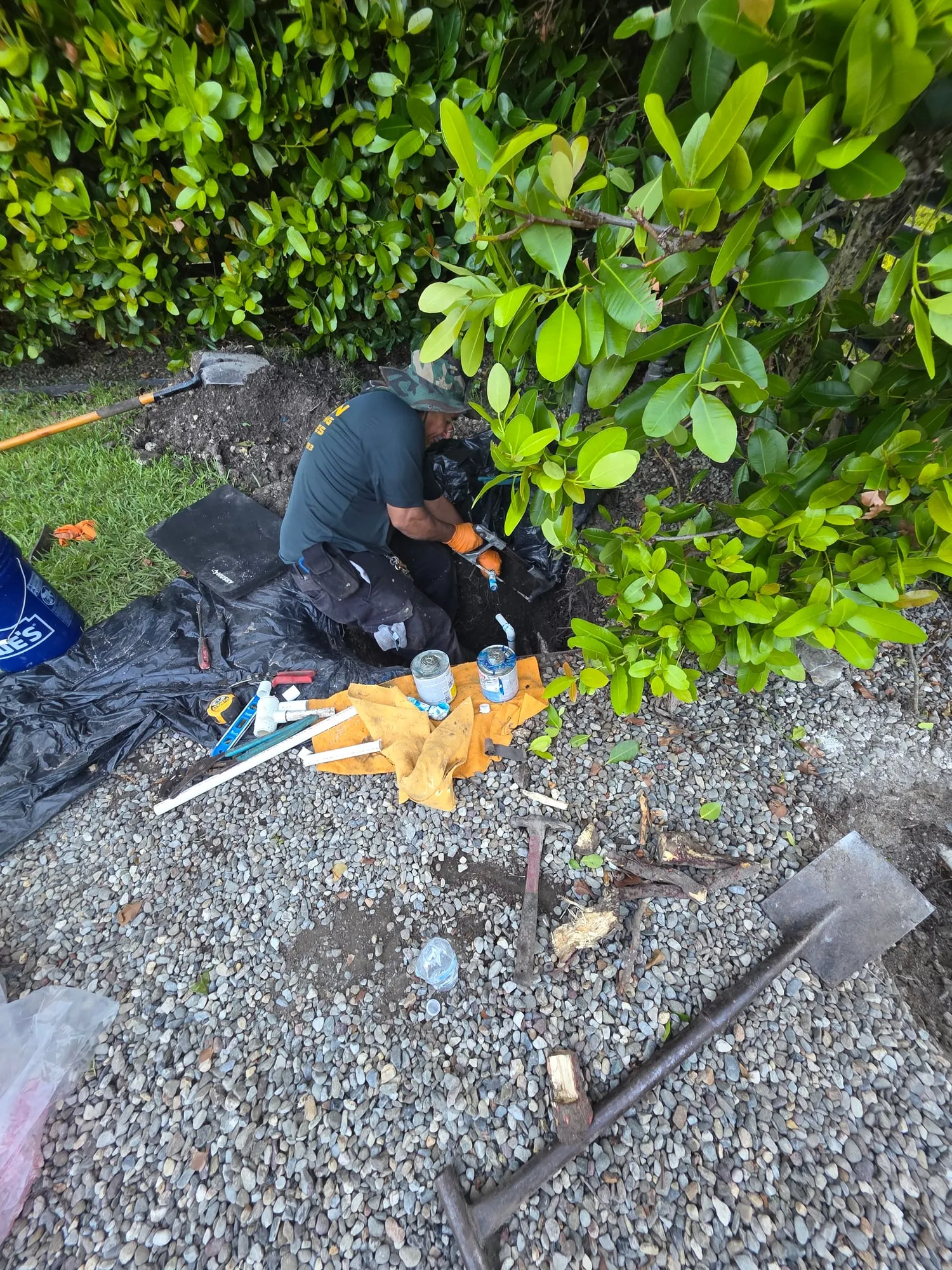 Plumber working in a trench beside a hedge to repair a water line